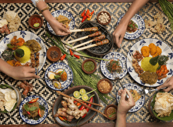 Traditional Balinese food served on patterned plates, featuring satay, yellow rice, and local spices